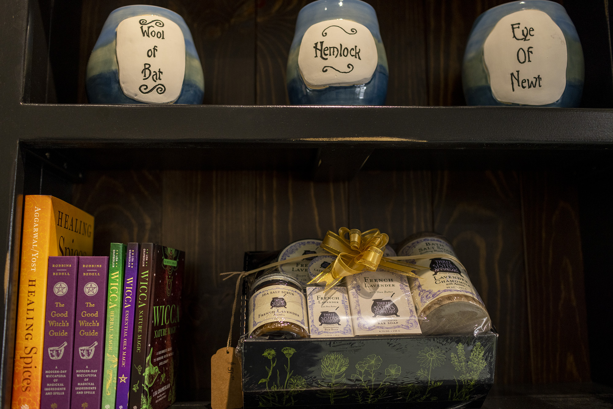 Decorative ceramic jars with the words wool of bat, hemlock, and eye of newt. Books on healing spices, which guide, and wicca. Three Sisters Apothecary French Lavender gift set with soaps, bath salts, and body butters.