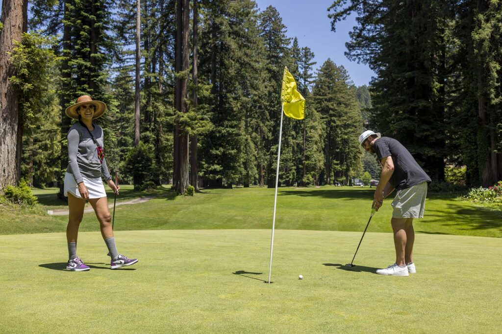 couple golfing at Northwood Golf. Golf course surrounded by redwood trees.