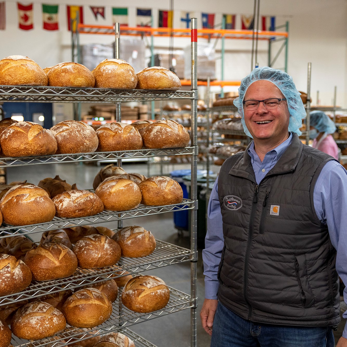 bakery owner standing next to racks of freshly baked bread. Costeaux French Bakery